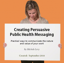 A woman holding a large sign in front of her with the course title, author, and date written on it.